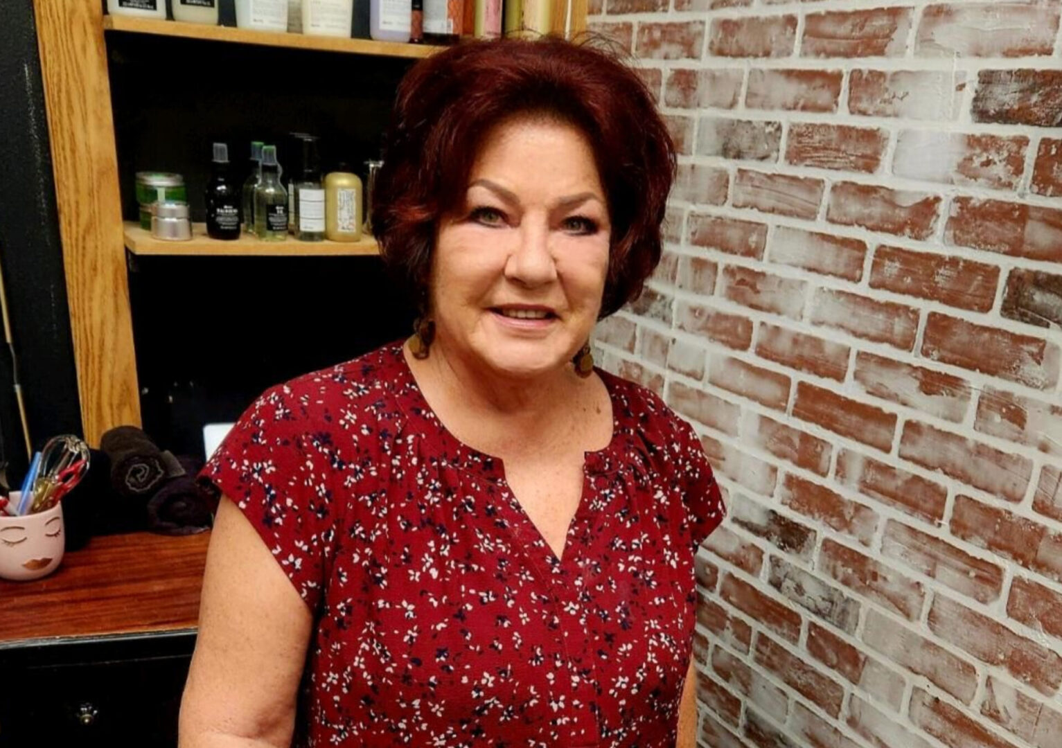 A woman with red hair standing in front of a brick wall.